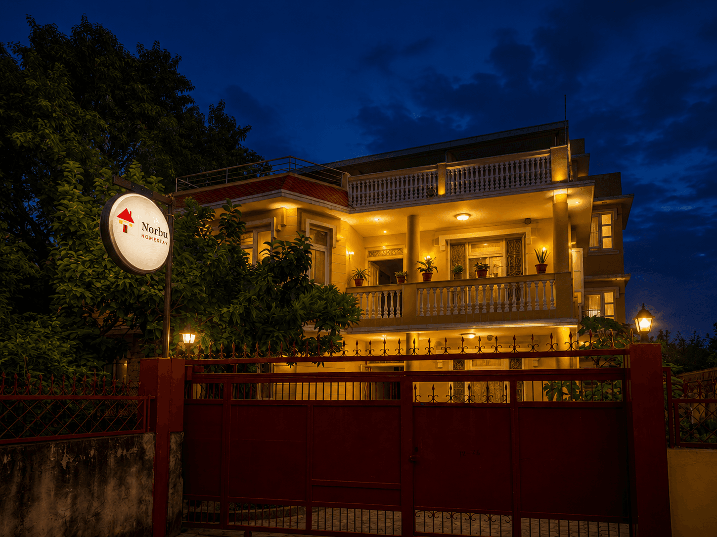 Norbu Homestay glowing warmly at night behind its red entrance gate